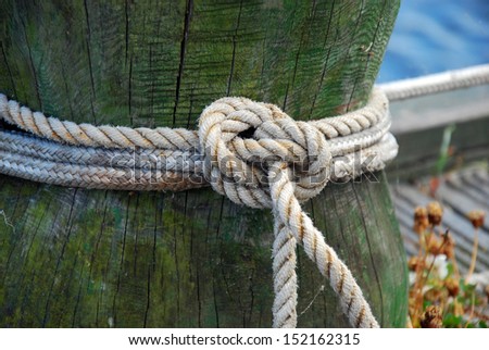old wooden mooring bollard with knotted rope in the ship port