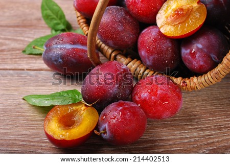 fresh wet plums falling out of a basket on wooden background
