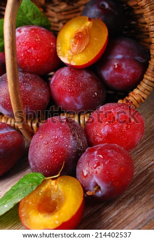 fresh wet plums falling out of a wicker basket on wooden background