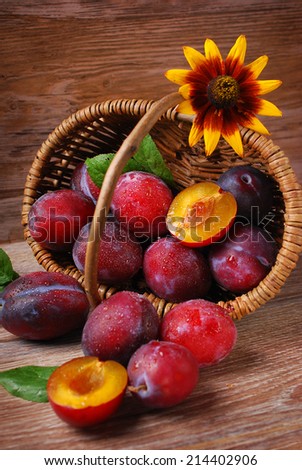 fresh wet plums falling out of a wicker basket on wooden background