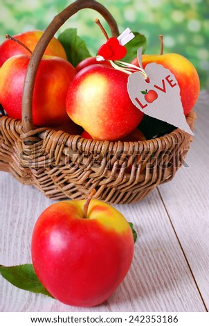 wicker basket full of red apples with hanging eco paper tag on wooden table in the garden