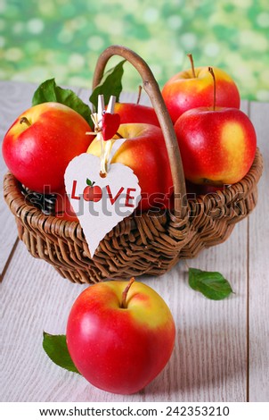 wicker basket full of red apples with hanging eco paper tag on wooden table in the garden