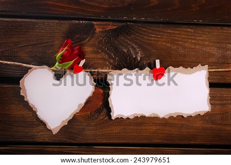 torn paper heart with red rose and card hanging on twine against wooden wall