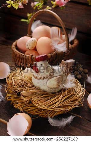 easter decoration of hen figurine in the nest and wicker basket with eggs on wooden background