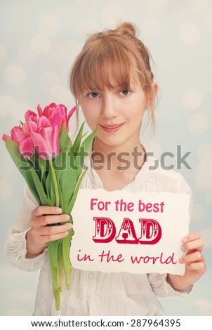 beautiful young girl giving bouquet of pink tulips and greeting card for dad on father`s day