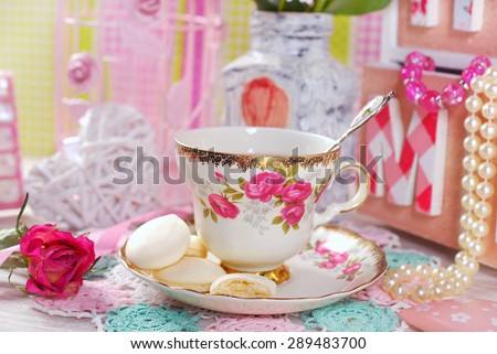 tea in fine china cup with roses ornament and anise meringue cookies in romantic style