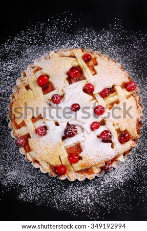 apple pie with cranberry and powdered sugar on black table