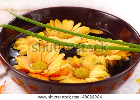 home spa with yellow flowers floating in bowl and drops of water on leaves