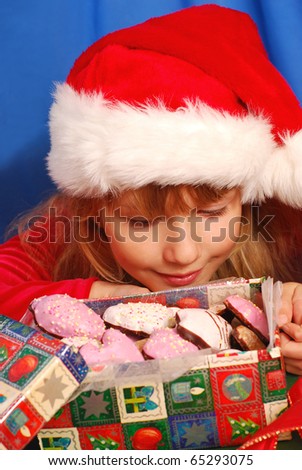 young girl in santa`s hat looking into the box with christmas ginger breads