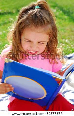 little girl reading a book in the garden sitting on the blanket