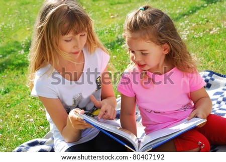 two sisters reading the book with fairy tales in the garden sitting on the blanket