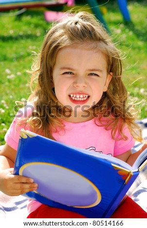 little girl reading a book in the garden sitting on the blanket