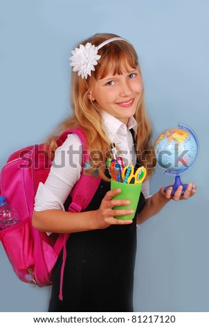 schoolgirl with pink backpack with globe and school supplies in hands against blue background