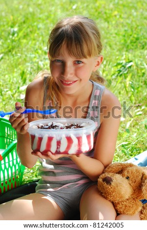 young girl eating big ice cream in box sitting on the blanket on the picnic