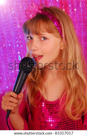 young girl in pink shiny dress singing with microphone on the stage