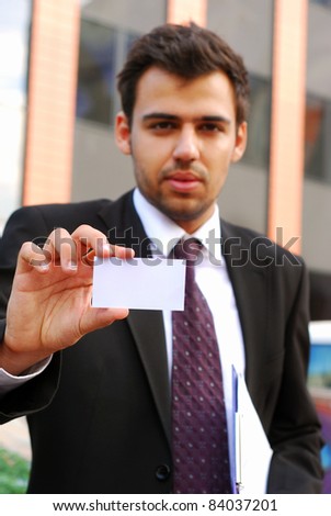 young businessman holding visit card in hand and standing in the front of office building