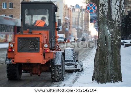 Tractor cleaning the road from the snow. Excavator cleans the streets of large amounts of snow in city. Workers sweep snow from road in winter, Cleaning road from snow storm.
