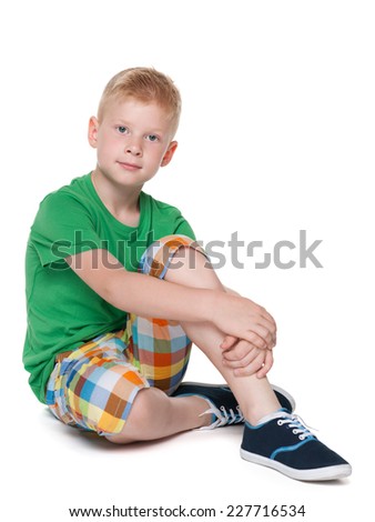 A smiling little boy in a green shirt is sitting on the white background