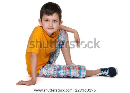 A smiling little boy in a yellow shirt is sitting on the white background
