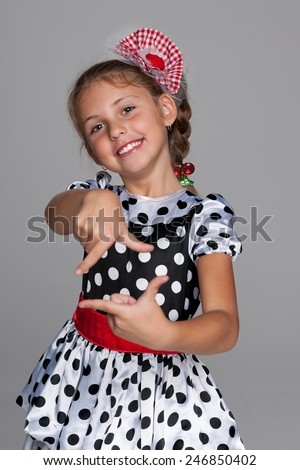 A smiling little girl makes a hands gesture against the gray background