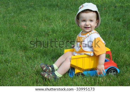 a smiling baby with a pacifier is sitting in the toy truck on the grass