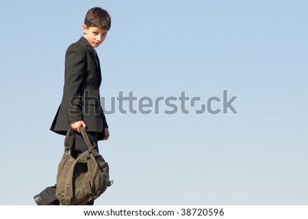 a happy boy is coming back from school holding his schoolbag in his hands