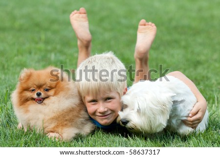 A smiling boy and his pets are lying on the green grass