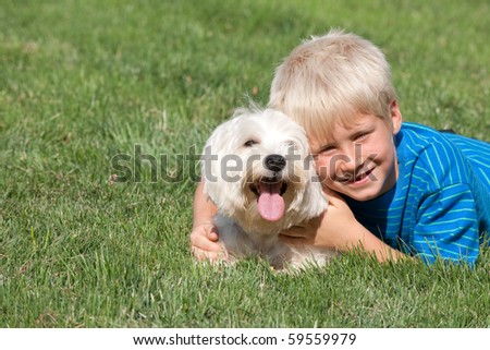 A lying on the grass smiling boy is hugging his pet
