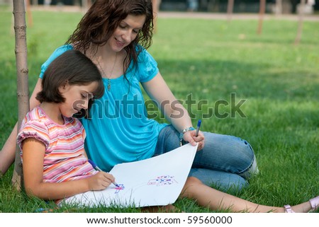 A portrait of a pretty smiling girl in pink sitting on the summer grass with her mother and drawing