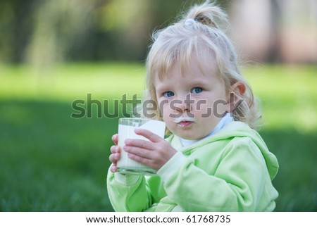A little girl dirty with milk is sitting in the green grass