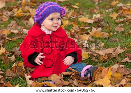 A closeup portrait of a little girl in red coat sitting among yellow leaves in the autumn park