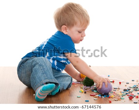 A toddler is playing with yarn, threads and buttons sitting on the wooden floor; isolated on the white background
