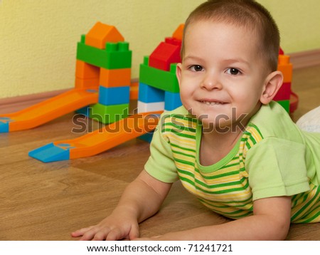 A little boy is lying on the wooden floor at the toy car track