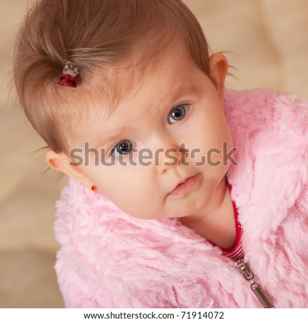 A closeup portrait of a cheerful little girl in a pink fur coat