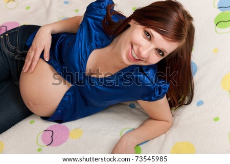 A cheerful pregnant woman lying on the sofa is holding her belly with her hand