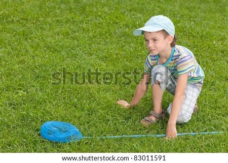 A boy with a butterfly net is sitting on the summer lawn