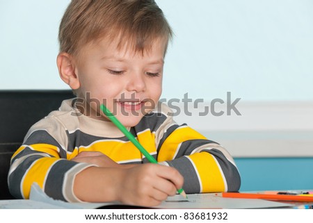 A little smiling boy draws at the desk