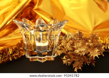 Lit candle in a transparent glass candlestick on a festive gold glitter background with Christmas decoration