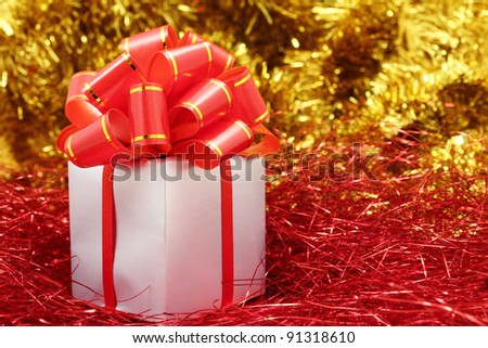 Silver gift wrapped present with red bow on a festive red and gold glitter background