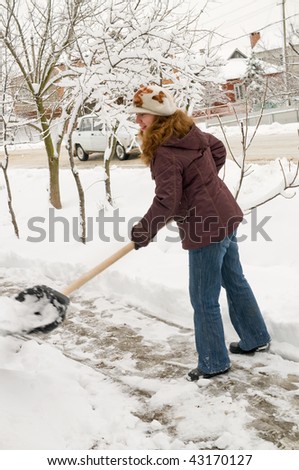 The young woman cleans snow from sidewalk.