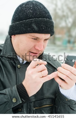 In the winter in the street the man enters the information into a mobile phone.