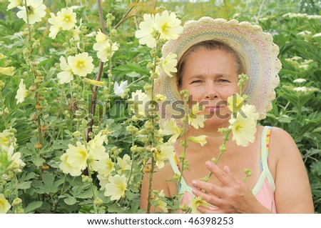 The elderly woman in a summer hat on the fringe of the forest and wild-growing flowers