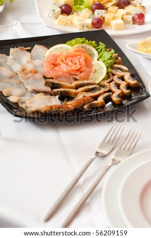On a black square plate the fillet of the prepared salmon and other fish delicacies are cut.