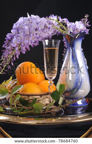 On a round little table a basket with oranges, white wine and a flower Wisteria.