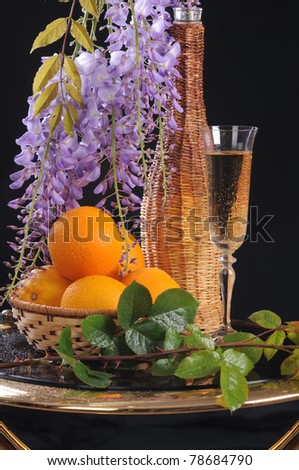 On a round little table a basket with oranges, white wine and a flower Wisteria.