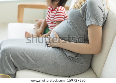 A pregnant woman and the boy who sit down on a sofa