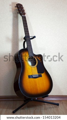 six-string acoustic guitar on a stand on light background