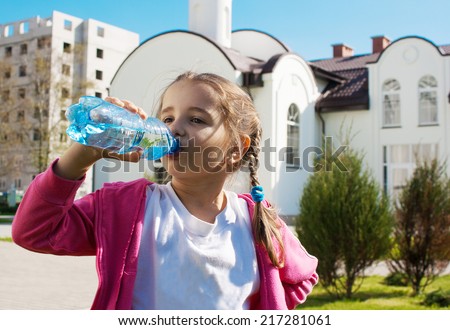 girl drinks water from a plastic bottle on sunny summer day