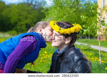 daughter kisses mom on spring day in the park. her mother wore on her head a crown of dandelions