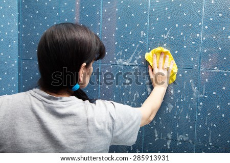 woman in a gray shirt washes blue tile with a cloth with soapy foam in the bathroom